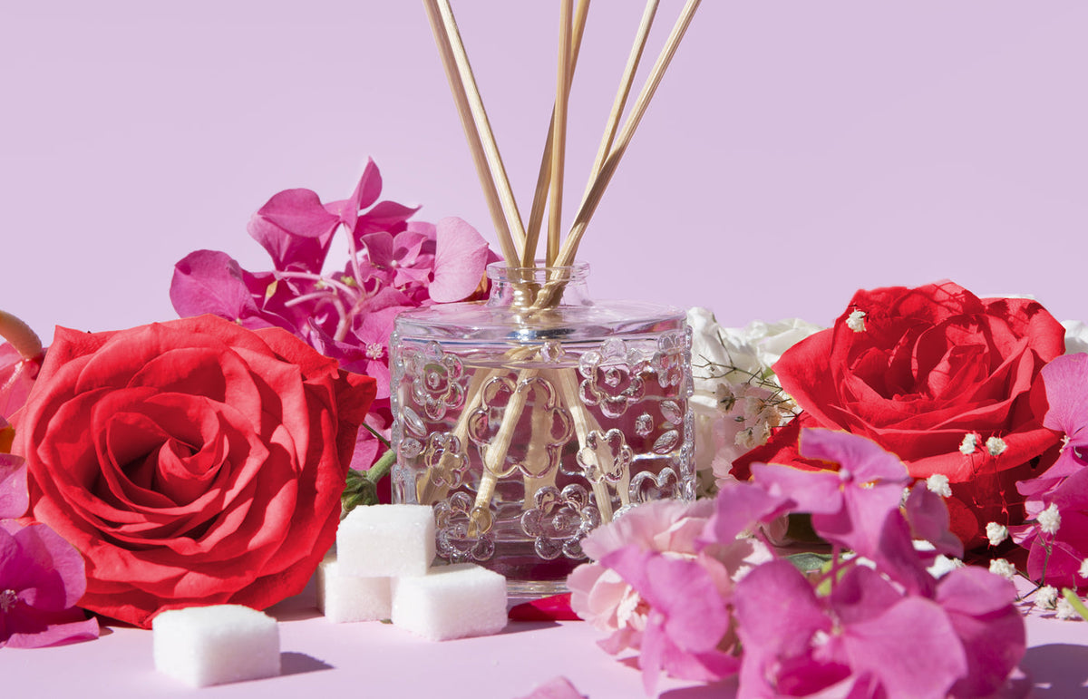 The Sugared Rose diffuser among pink orchids, red roses and sugar cubes on lilac