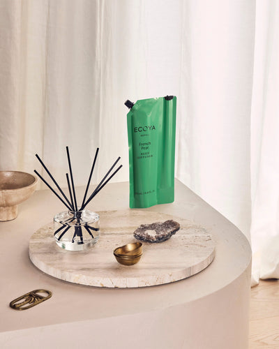 Ecoya French Pear reed diffuser with its green refill pouch on a travertine tray