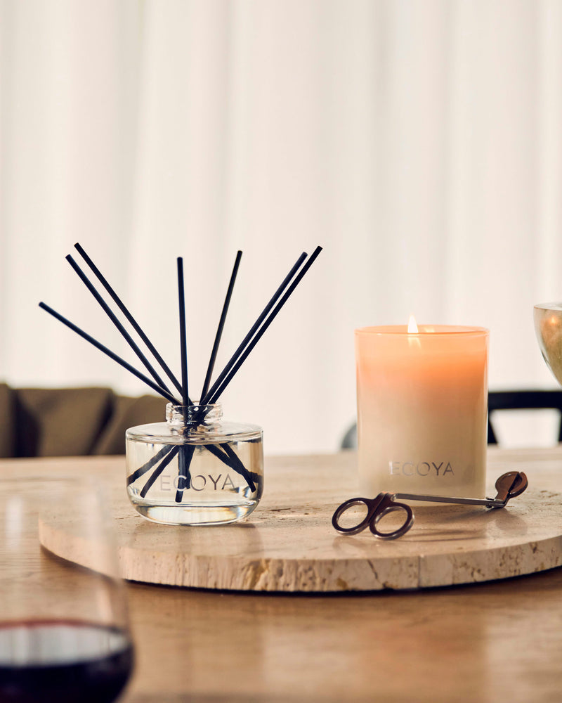 Ecoya reed diffuser and candle on a travertine tray by sheer curtains