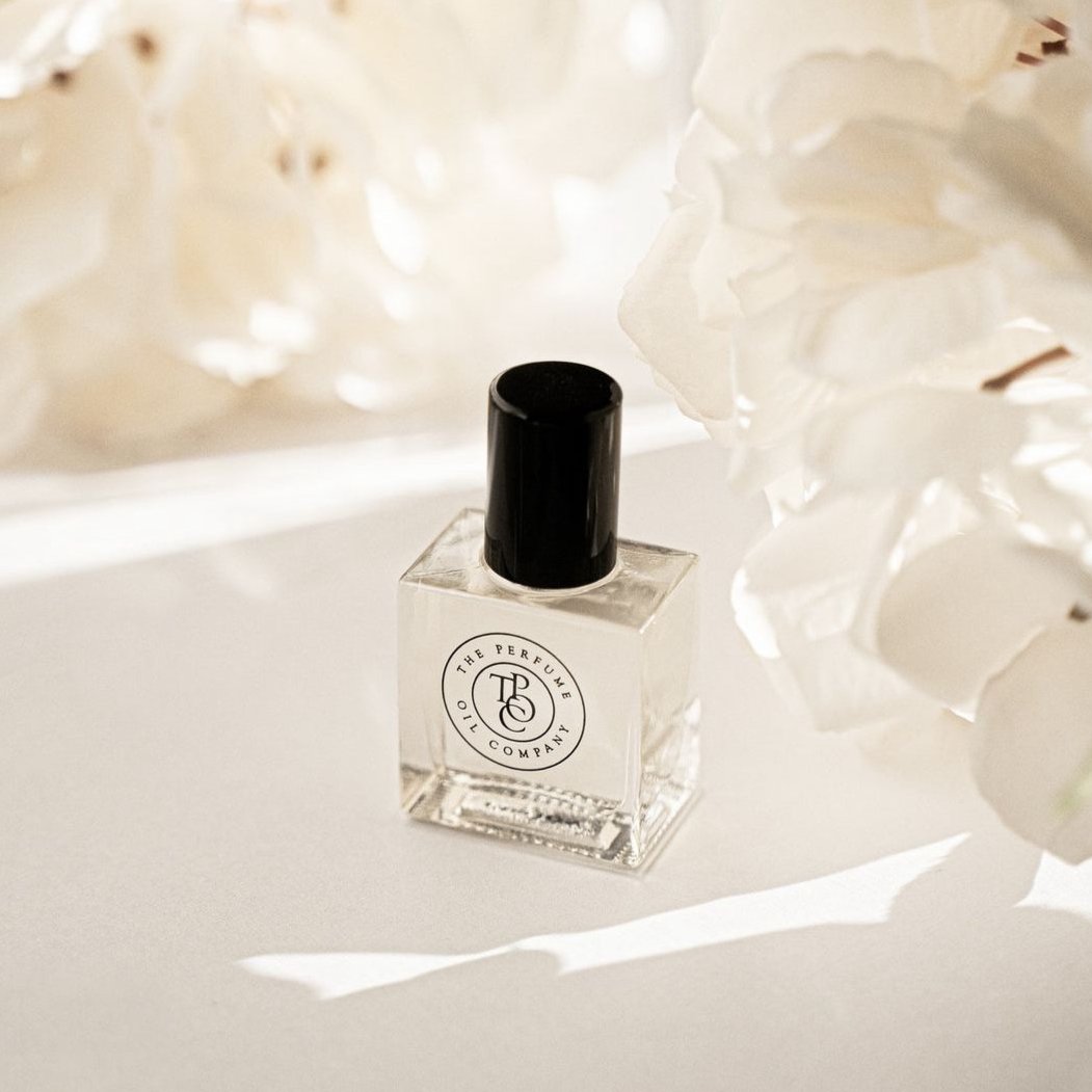 Perfume oil bottle with a black cap photographed in front of white blossom
