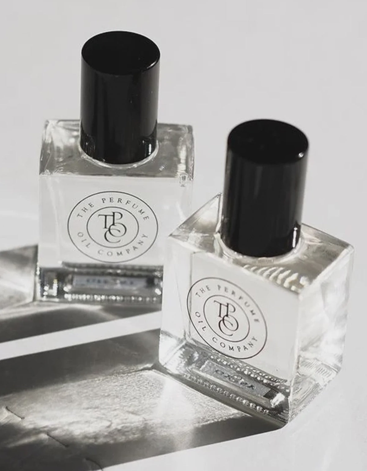 Two clear perfume oil bottles with black caps photographed close up on a pale background