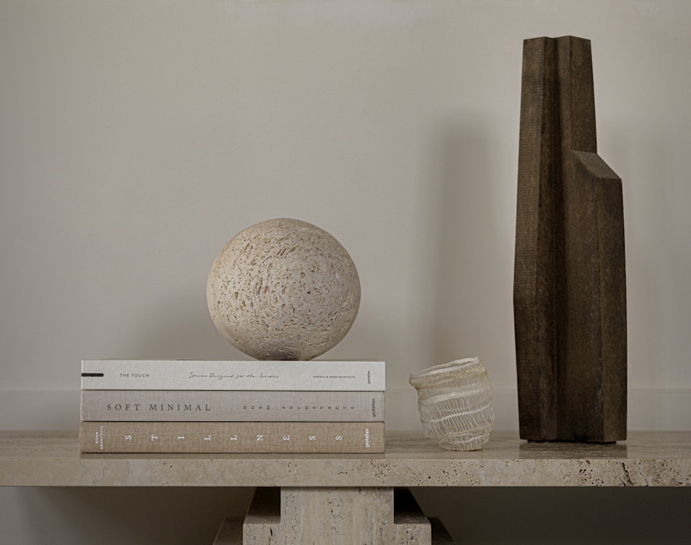 Neutral design books stacked on a stone bench beside a sphere and a dark timber vase
