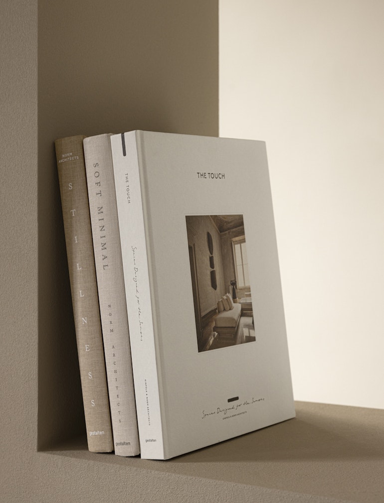The Touch hardcover standing upright with two other neutral design books against a warm wall