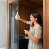 A woman cleaning a glass shower door with the Good Change bathroom spray bottle.