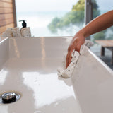 A person cleaning a sink with a Good Change reusable bamboo towel.