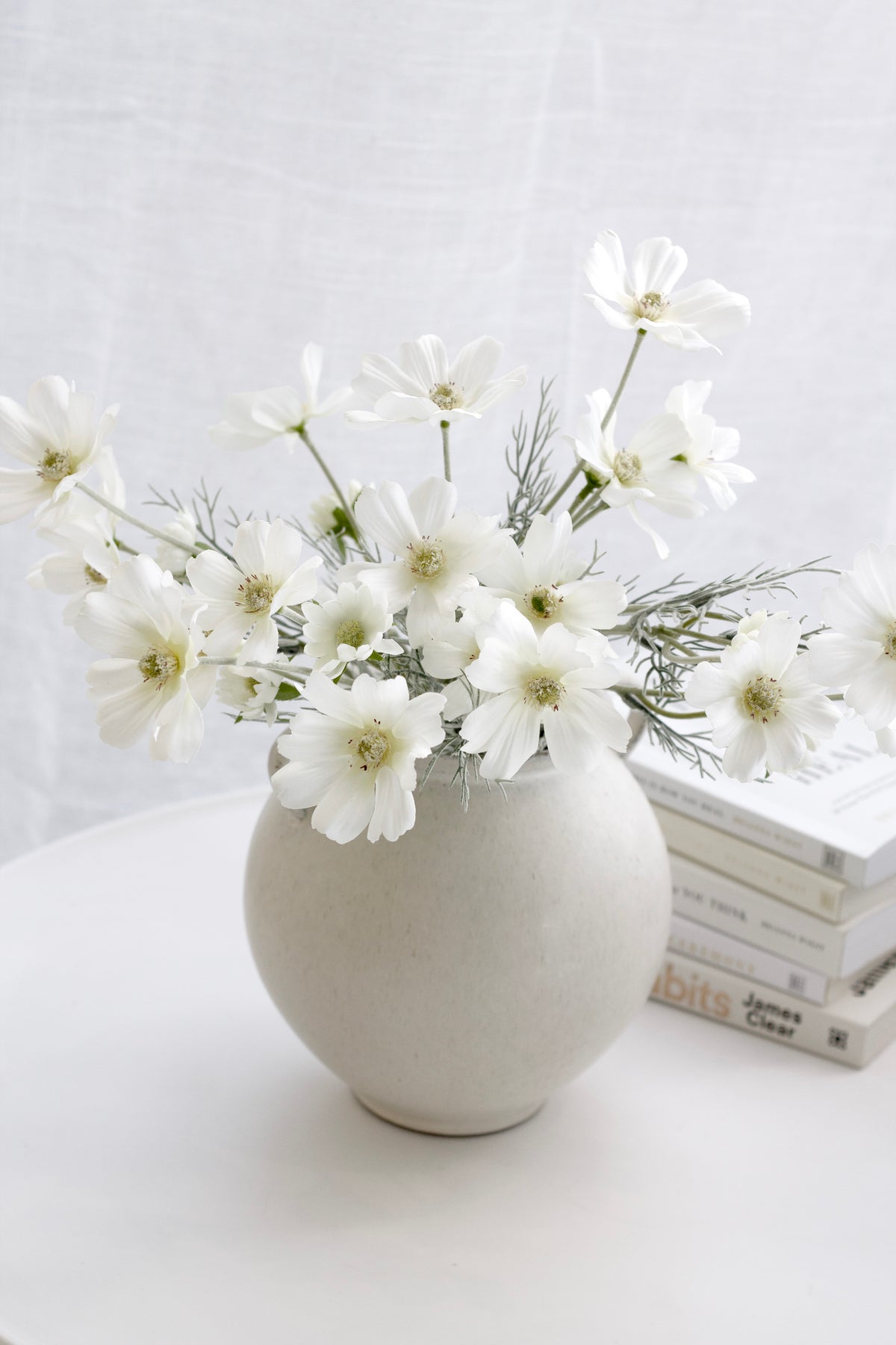 White faux cosmos in a rounded cream vase on a pale bench