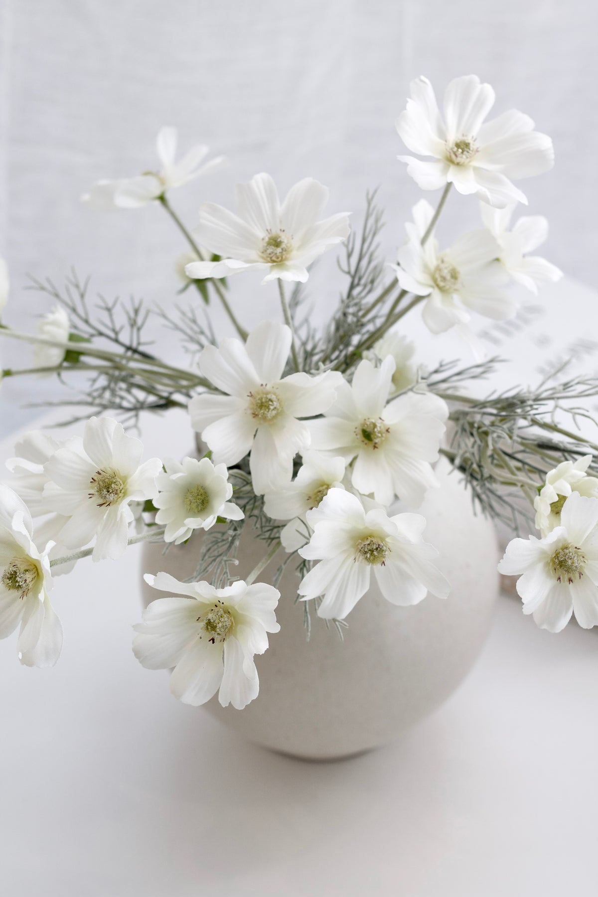 White faux cosmos spilling from a cream vase in soft light