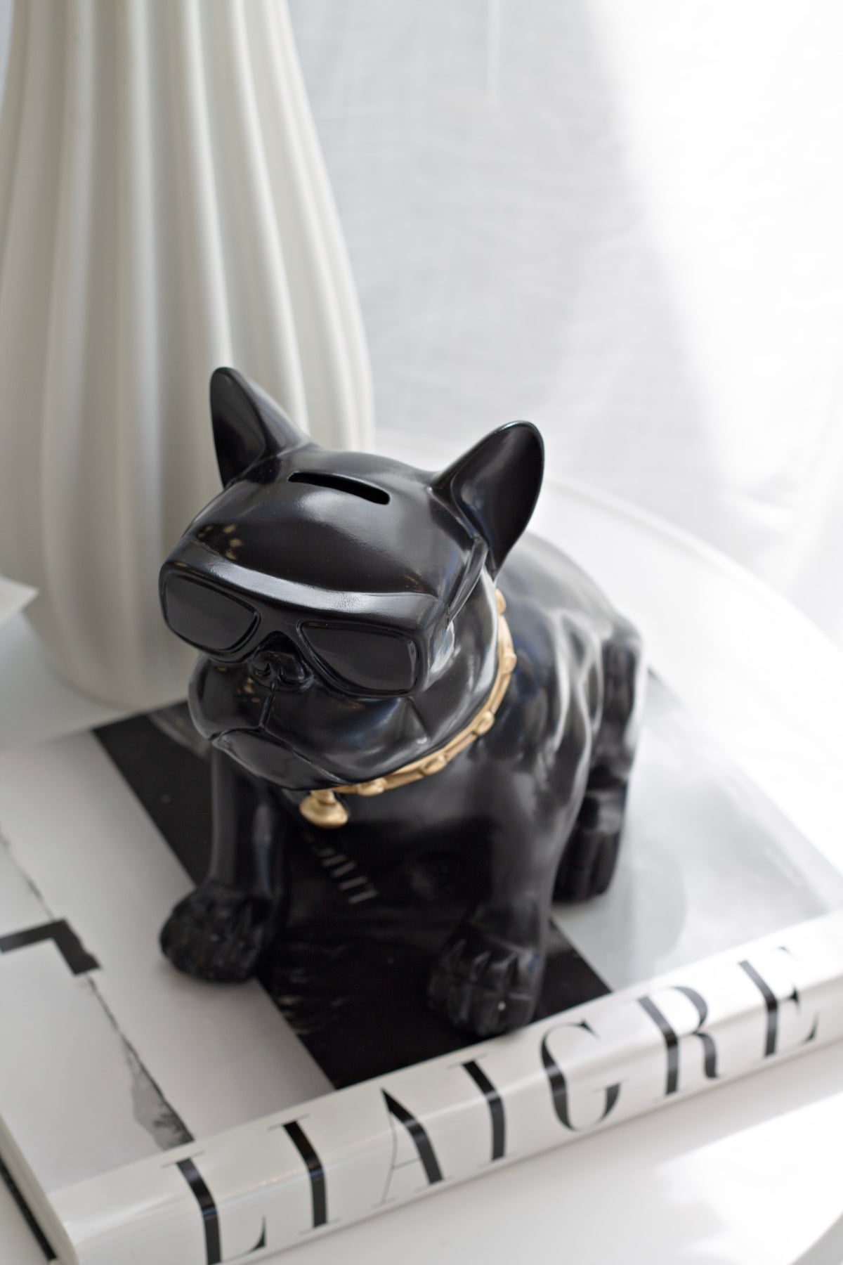 Frenchie on a book stack by a window, the coin slot visible along the top of its head