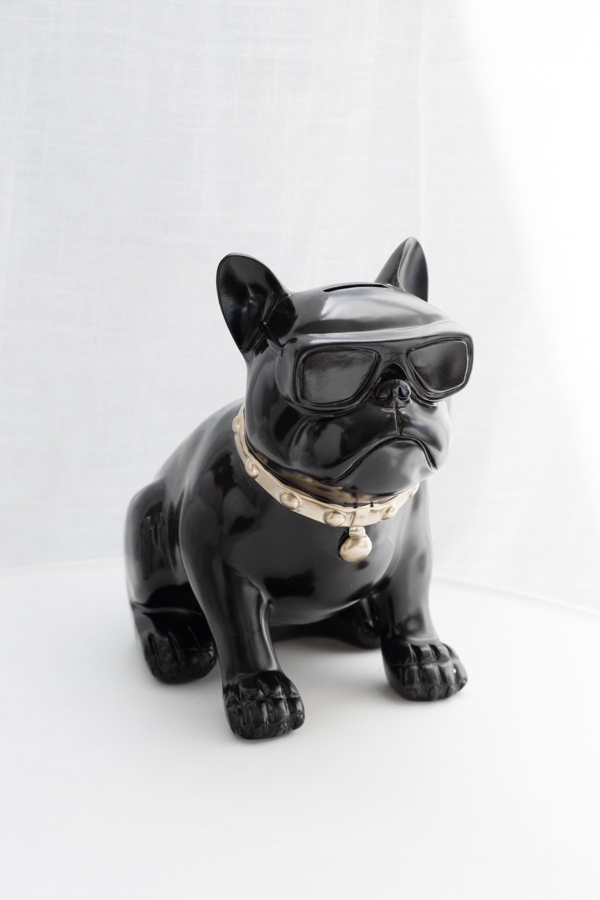 Black frenchie figure seated against a plain pale backdrop, sunglasses and collar in view