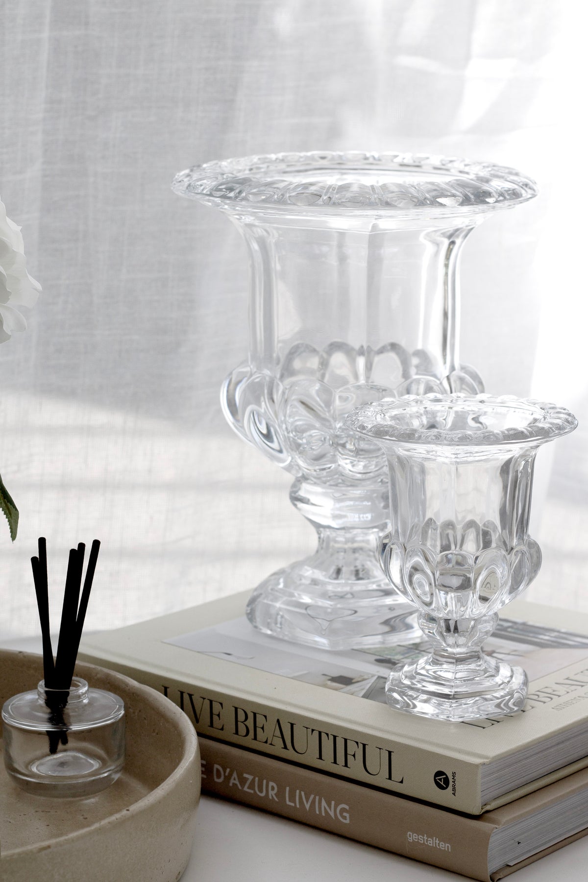 Omari glass urn vases in both sizes on stacked books beside a reed diffuser