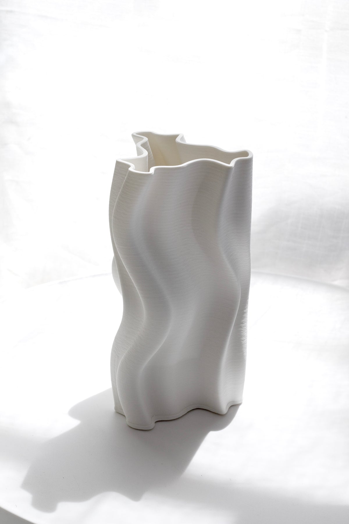 Arti vase standing empty against a pale draped backdrop, shadow falling to the right