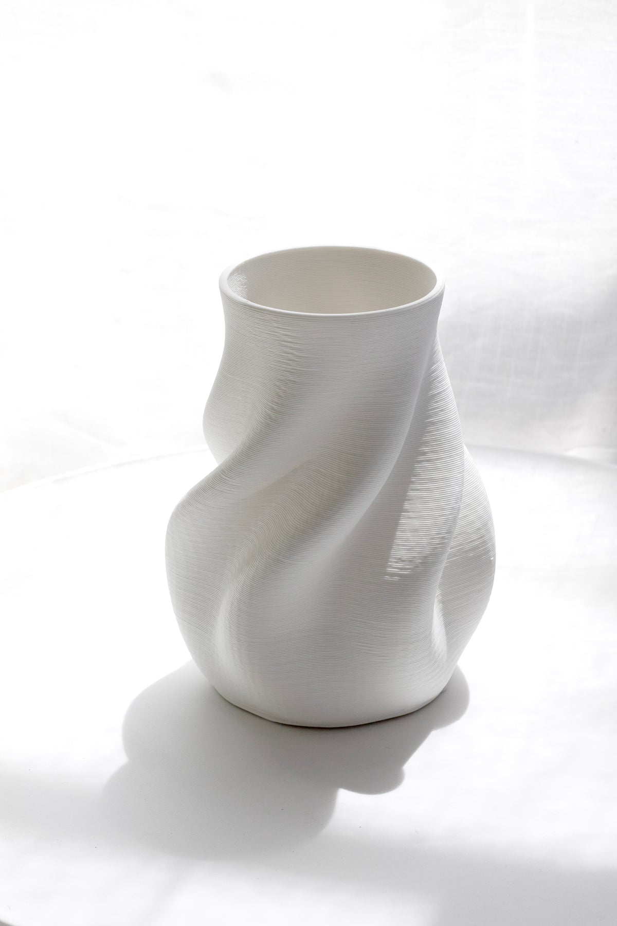 Bella white vase on rumpled linen in strong sunlight, its swirl casting a soft shadow