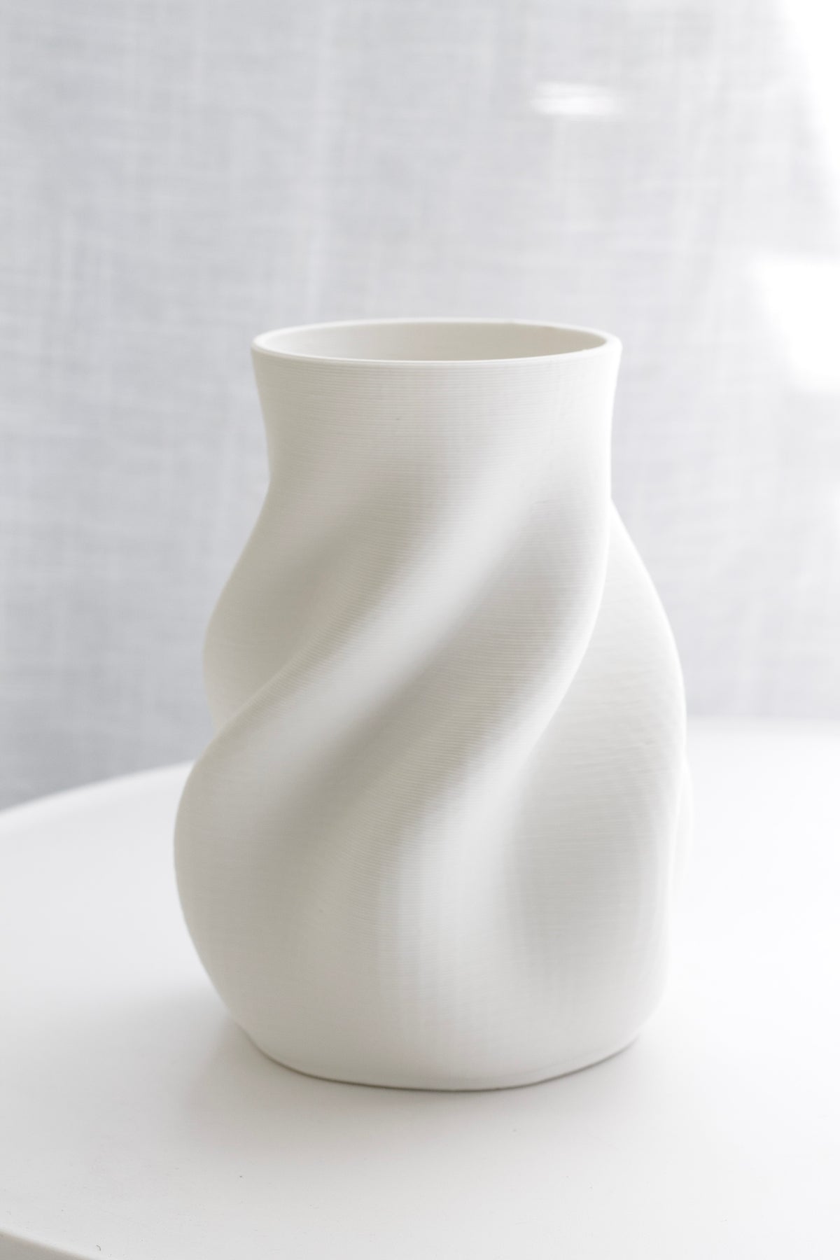 Bella white vase on a round white table against a linen curtain