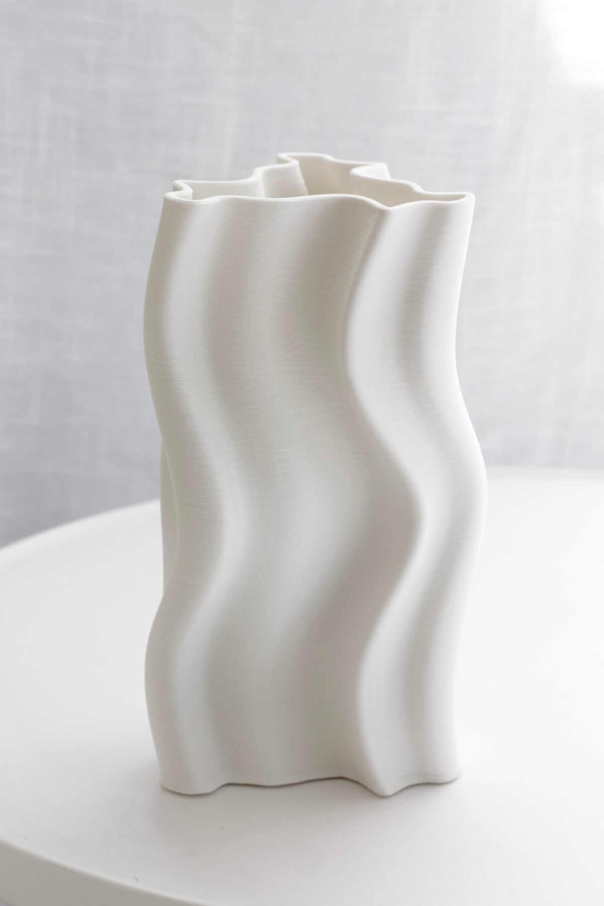 Arti vase on a white table with a linen curtain behind, waves running the full height