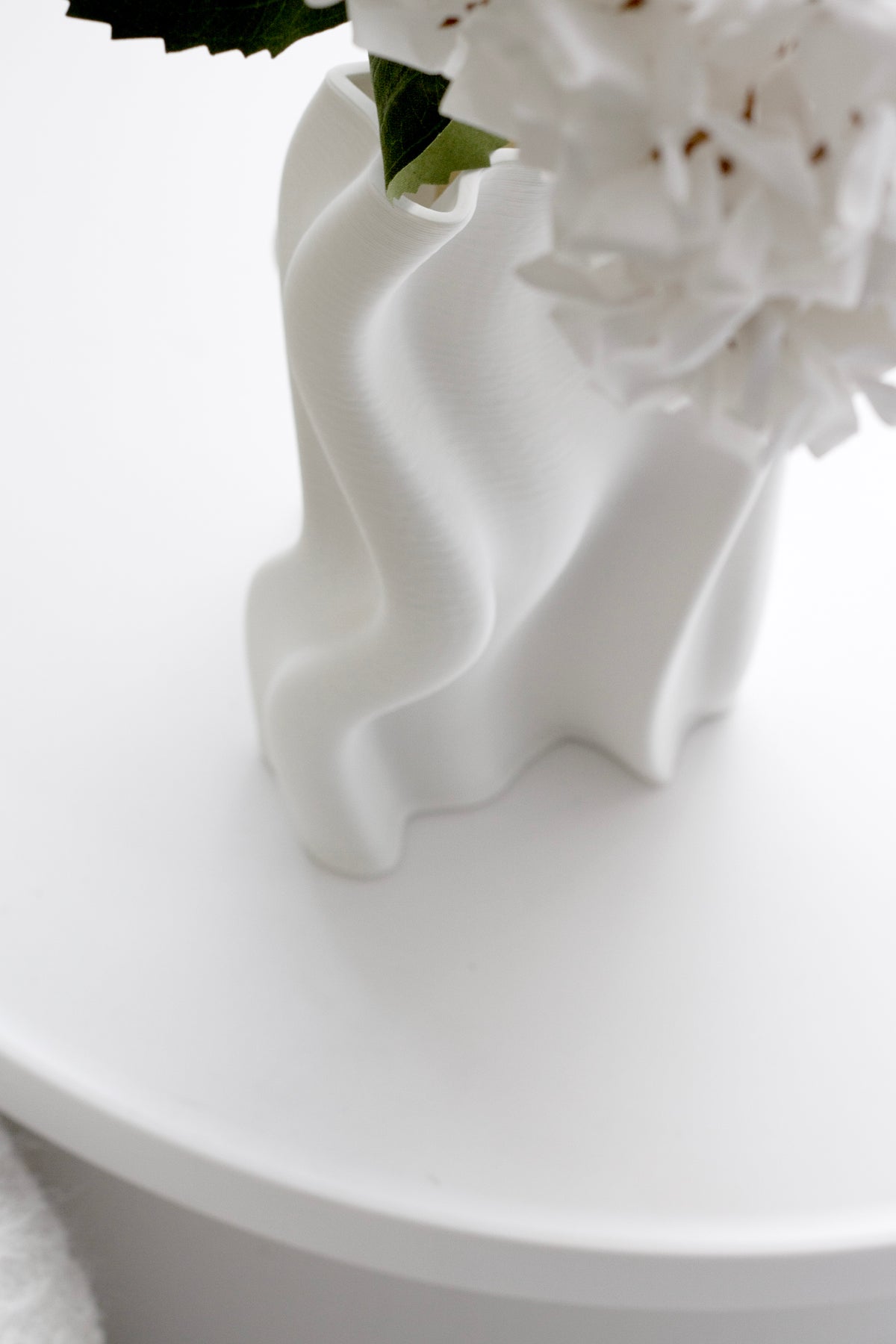 White blooms in the small Arti vase on a round white table, wavy body catching light