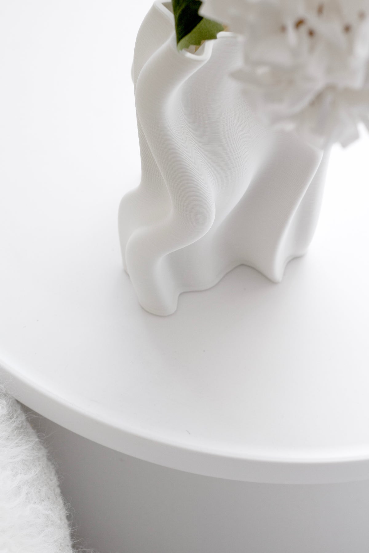 Small Arti vase of white flowers seen low across the edge of a round table