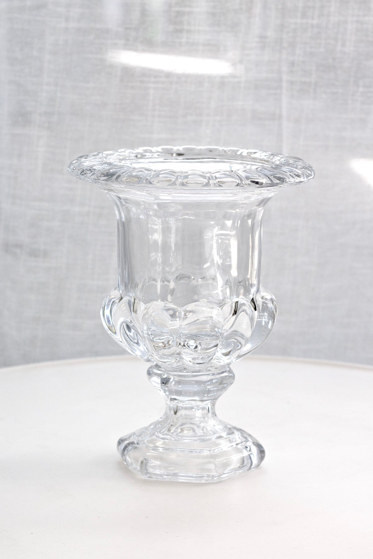 Omari clear glass urn vase on a white surface against a linen backdrop