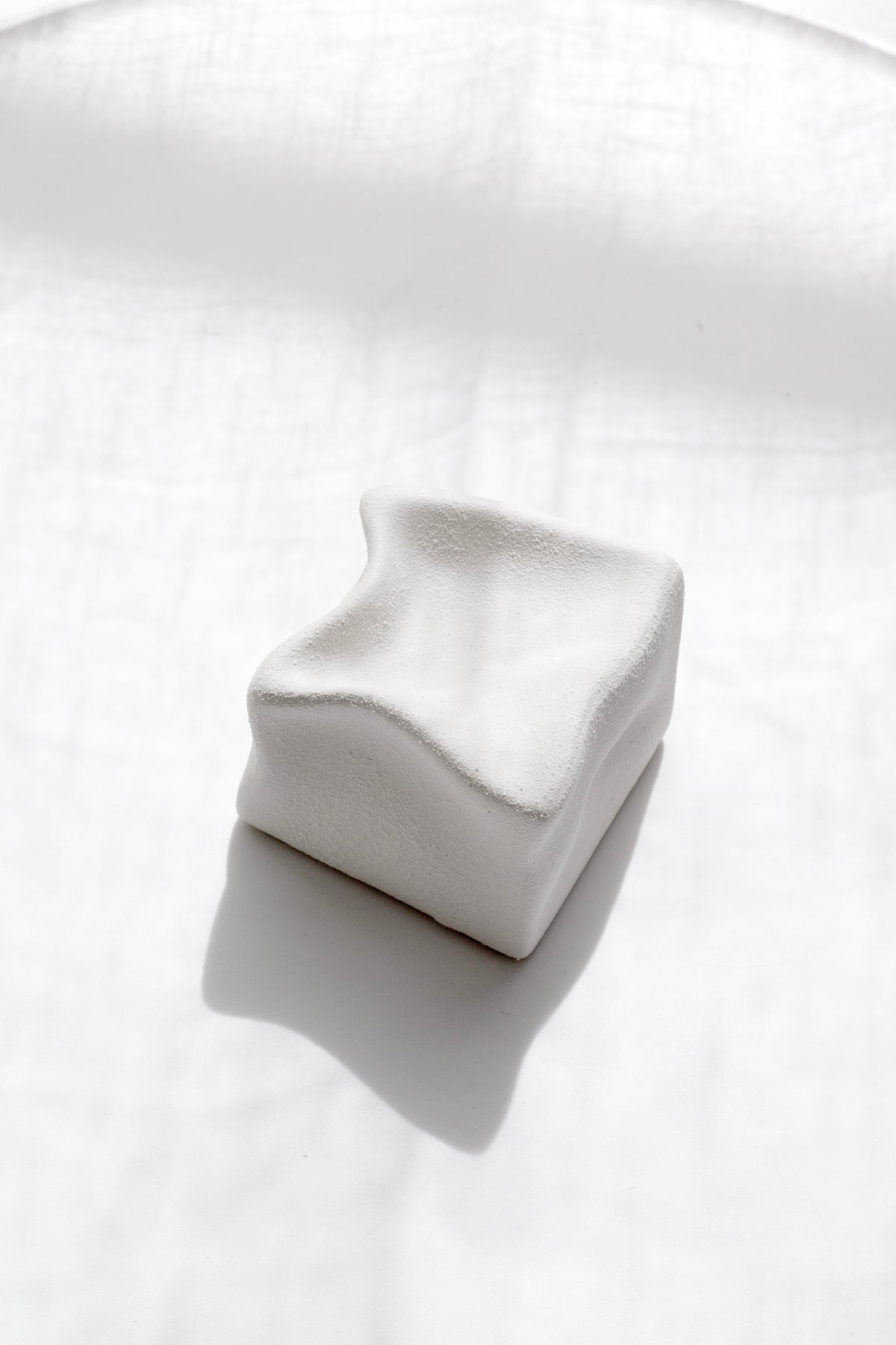 White Cubic Crush cube resting at an angle on rumpled linen with a soft shadow