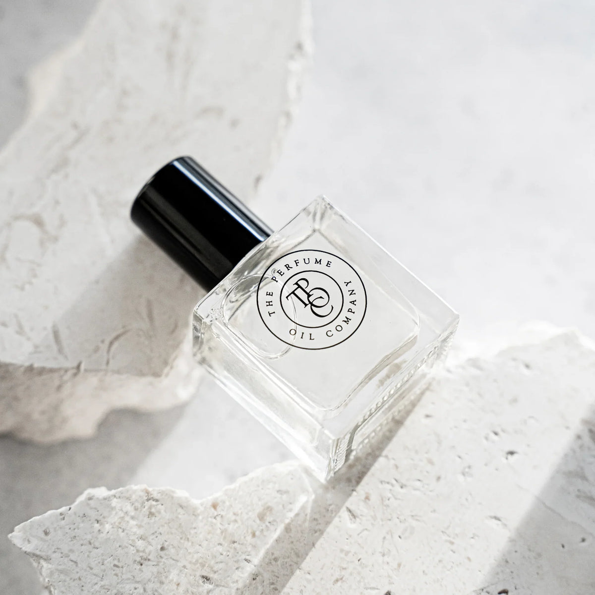 Perfume oil bottle on a white stone slab beside textured rock