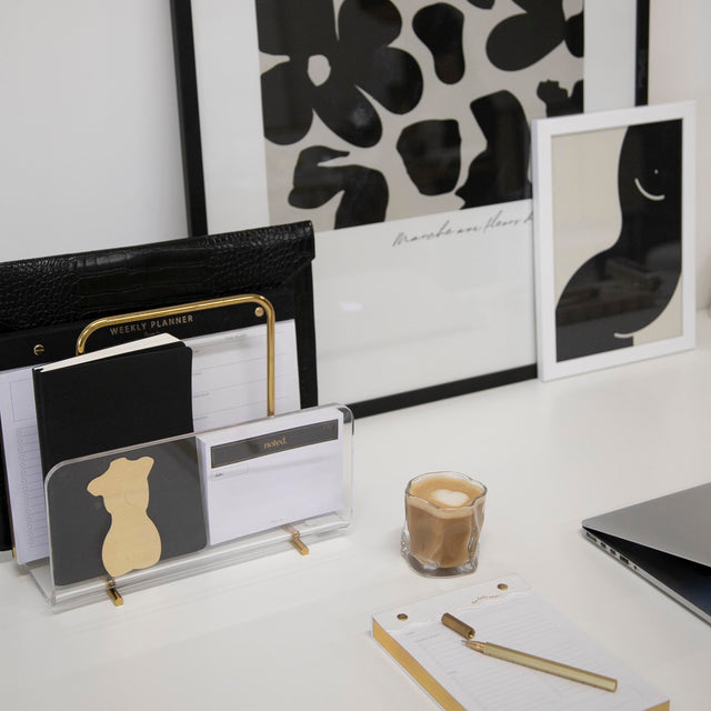 A black and gold desk with a laptop, Papier HQ Acrylic Gold Document Holder, and other items.