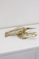 A Flux Home brass Lobster Ornament - Gold on top of a white cabinet with height.