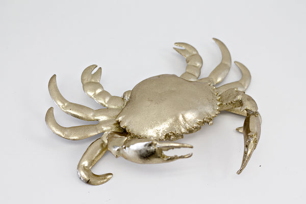 A Flux Home Crab Ornament - Gold lying on a white surface with depth and height.