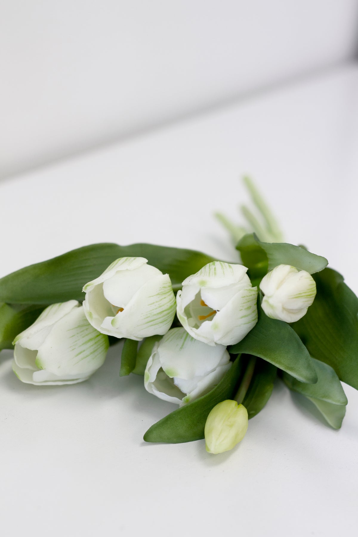 White faux tulip bunch with green leaves lying on a white surface
