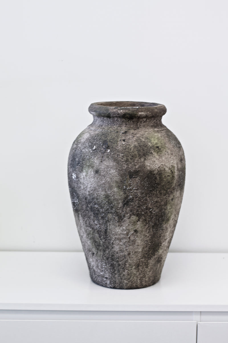 A Rustic Urn Vase by Flux Home sitting on a white table.