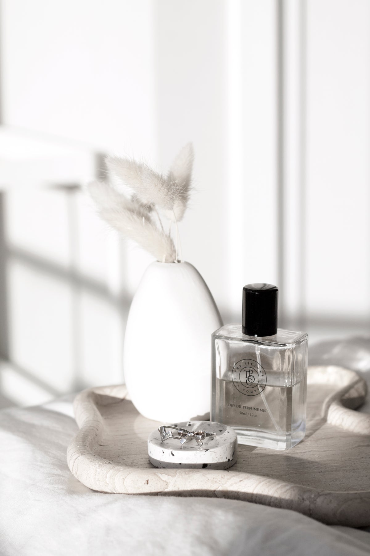 A sustainable-conscious customer's TRAVERTINE CURVED TRAY displays a bottle of perfume on a bed.