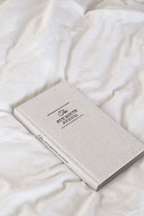 A white notebook on a bed with white sheets, where one can practice positive psychology and gratitude using the Intelligent Change's Five Minute Journal.