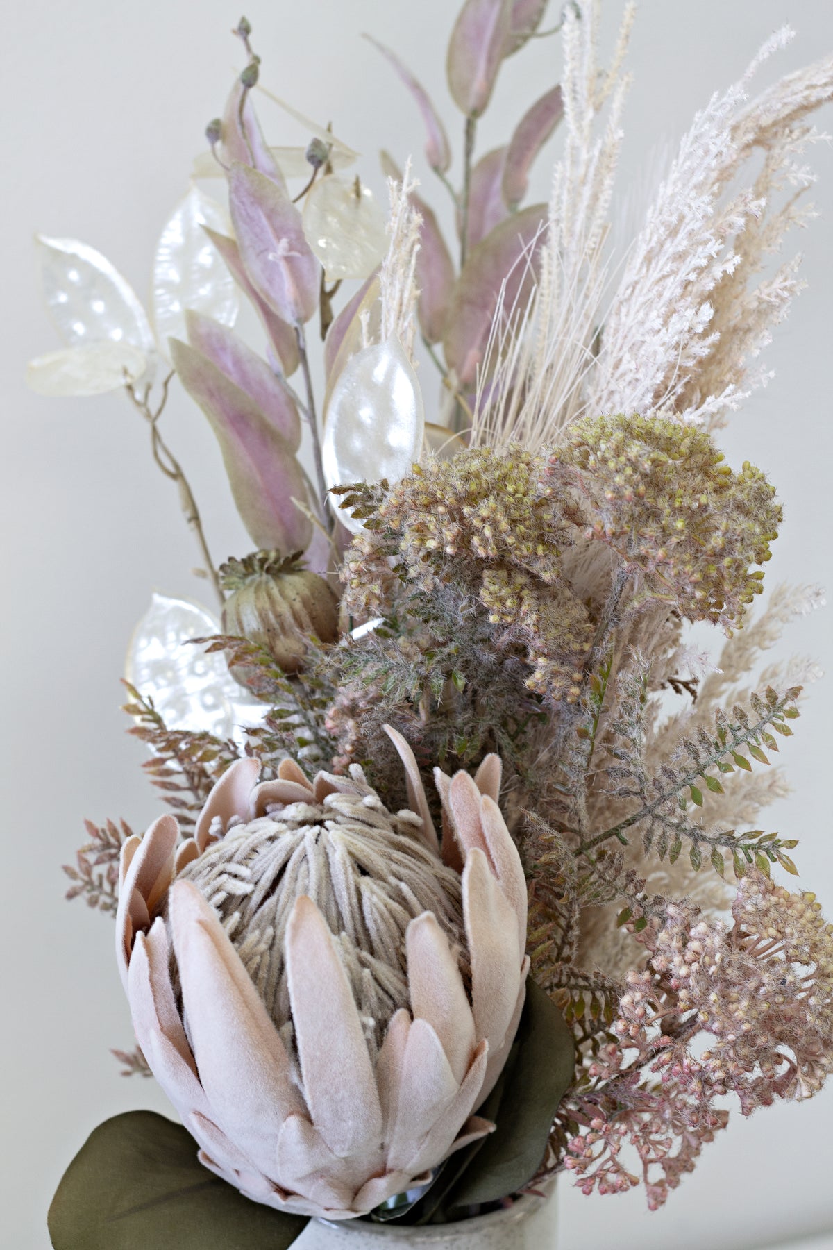 Pink protea with wild flower spray and dried grasses in a white vase