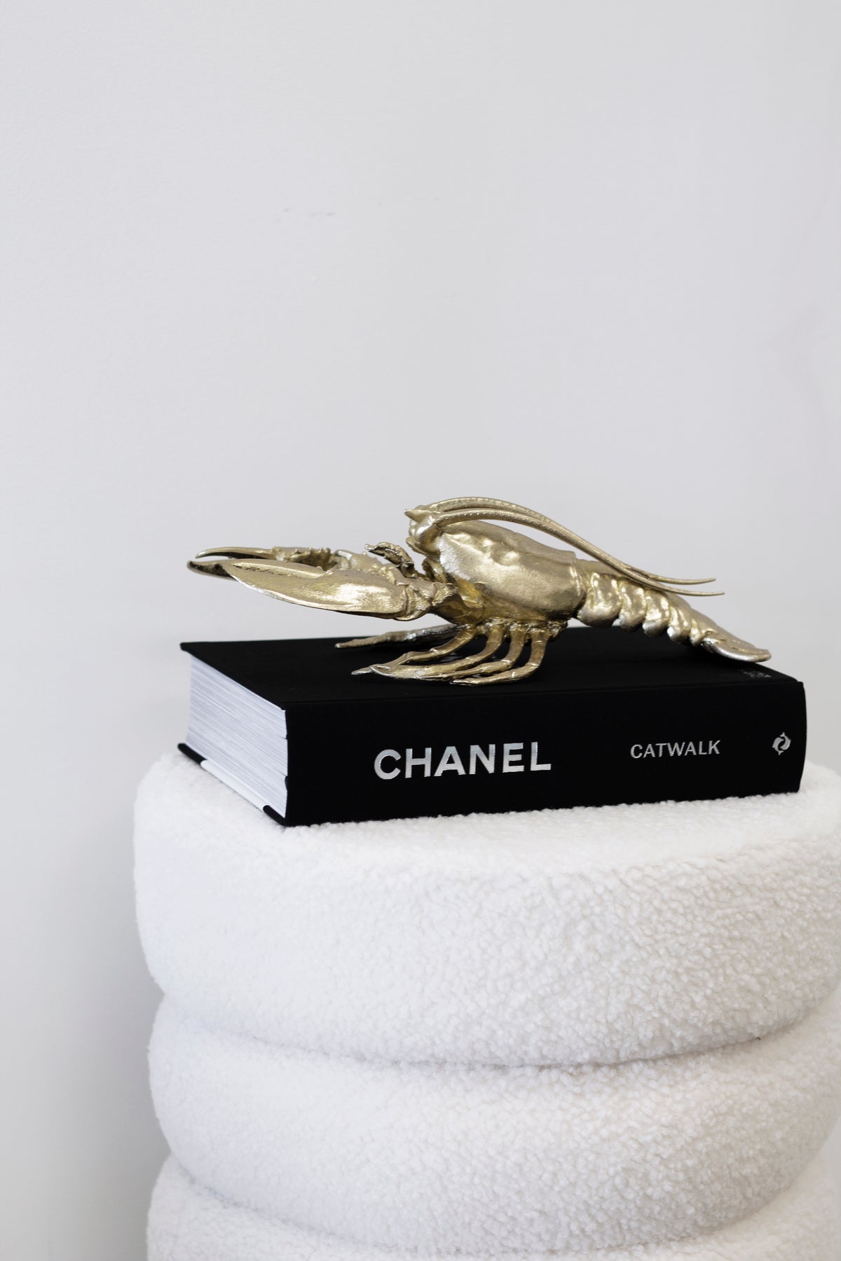 Chanel Catwalk book with a gold lobster ornament on top, on a white boucle stool