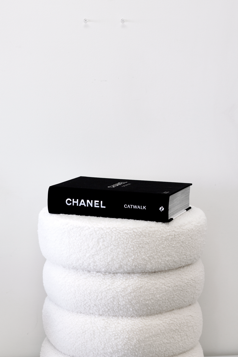 Books: "CHANEL CATWALK: THE COMPLETE COLLECTIONS" on top of a stack of towels, showcasing the iconic designs of Karl Lagerfeld and Virginie Viard.