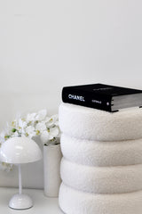 A Flux Home Baxter Boucle Ottoman - White / Black sitting on top of a white stool measuring 40x40x40 cm.