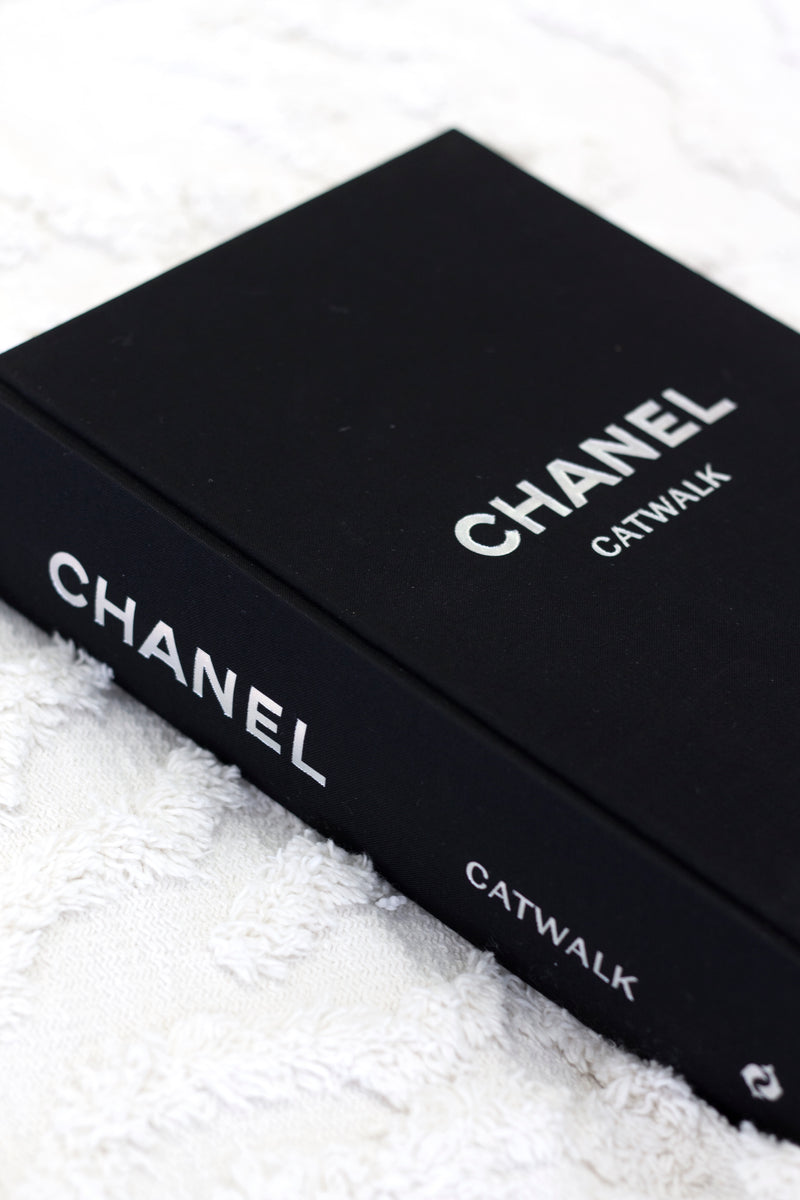 Books: CHANEL CATWALK: THE COMPLETE COLLECTIONS featuring beautiful design on a white bed.