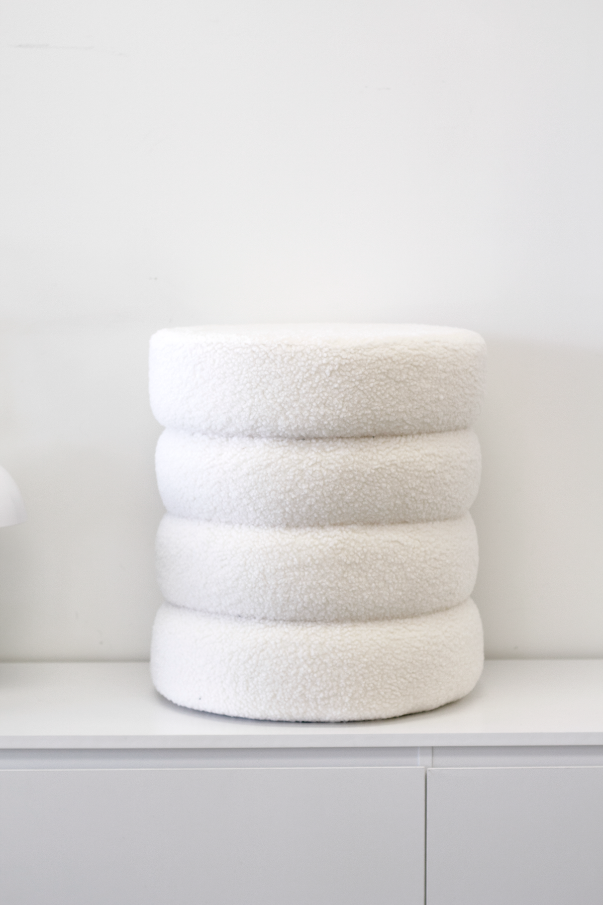 White tiered ottoman standing on a low white cabinet against a plain wall