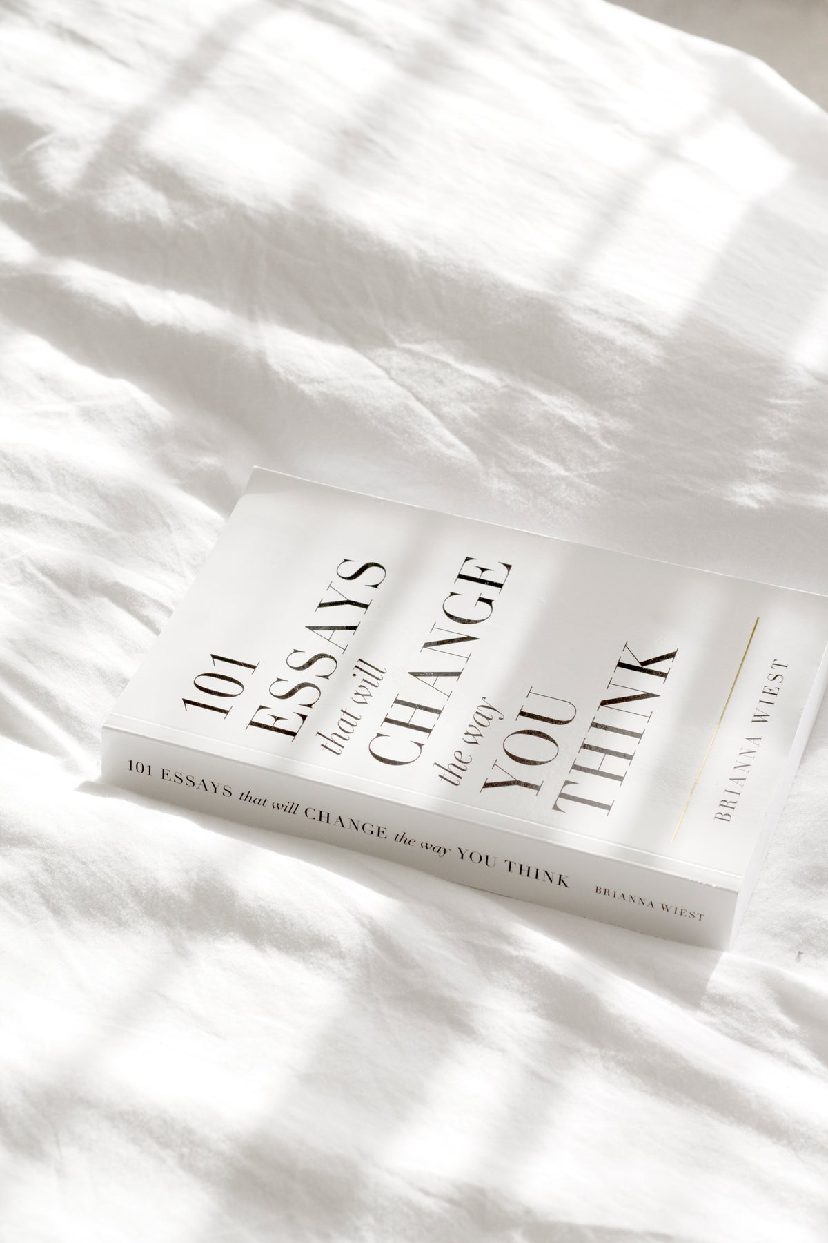 A bestseller book, 101 Essays That Will Change The Way You Think by Brianna Wiest, laying on top of a bed.