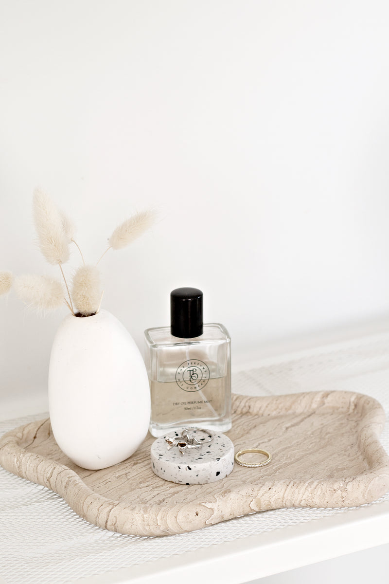 A small-sized Terrazzo Dimple Tray - Small Snow by Zakkia, with a bottle of perfume and a vase, featuring the ZAKKA Terrazzo design.