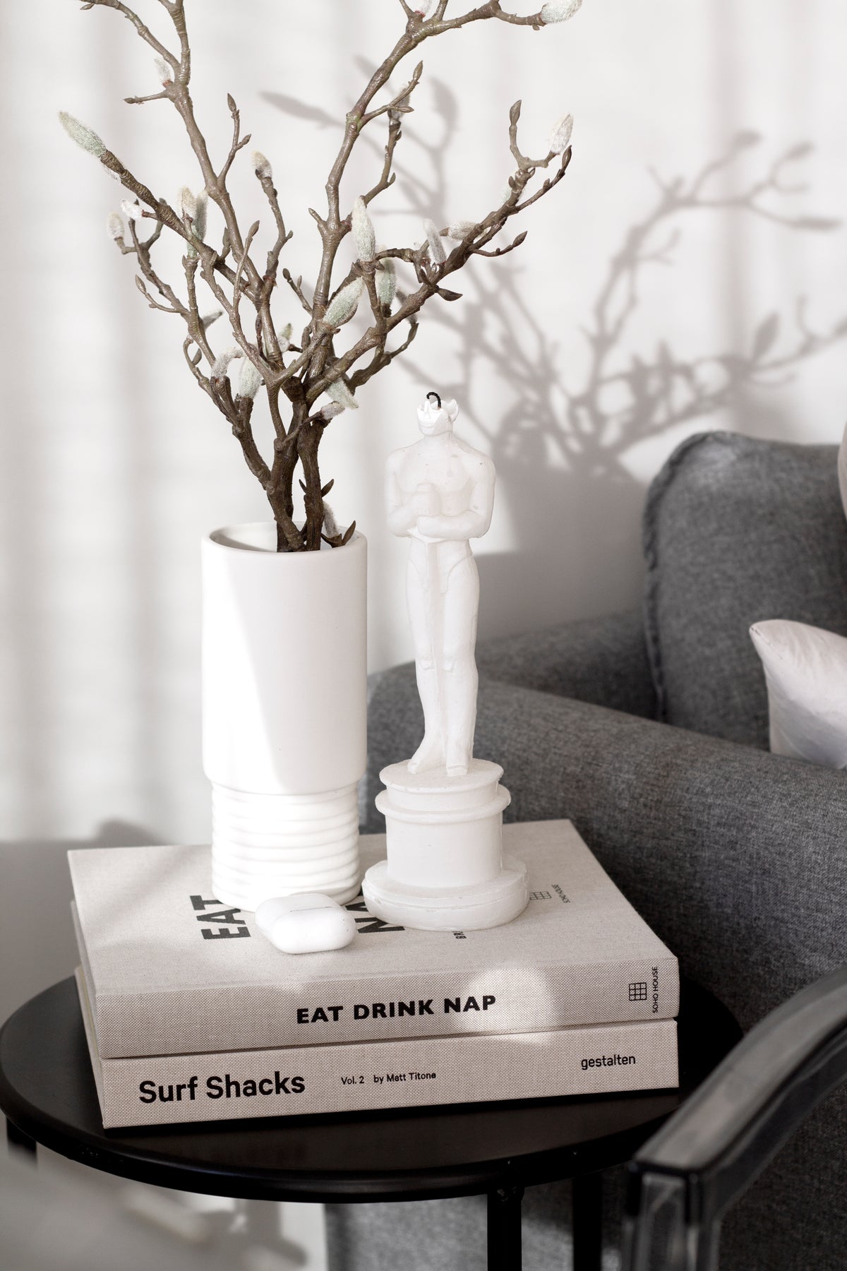 Surf Shacks Volume 2 in a book stack on a side table with a vase of branches and a white figurine
