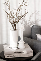 An Artificial Flora Magnolia Branch-filled white vase on a table next to a book.
