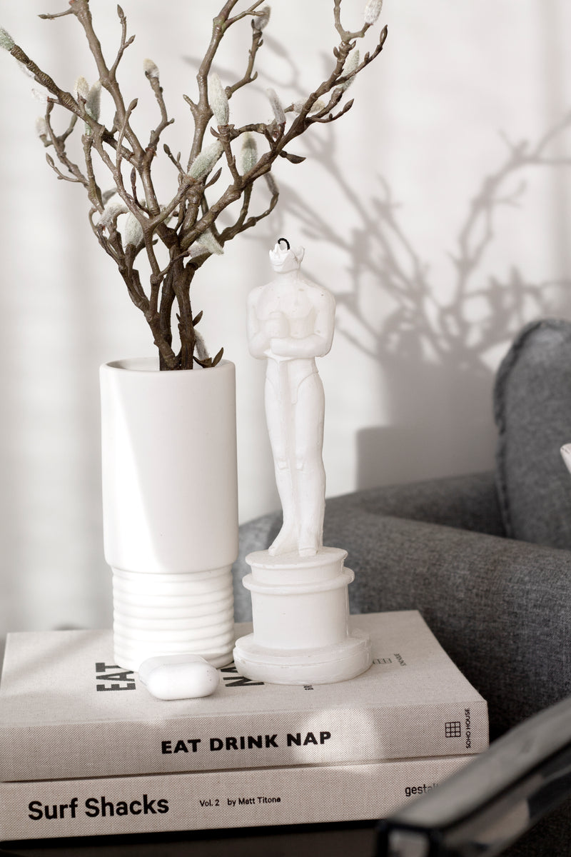 A Shooting Sparrow Oscar Sculpted Candle - Antique Silver sits on a table alongside books.