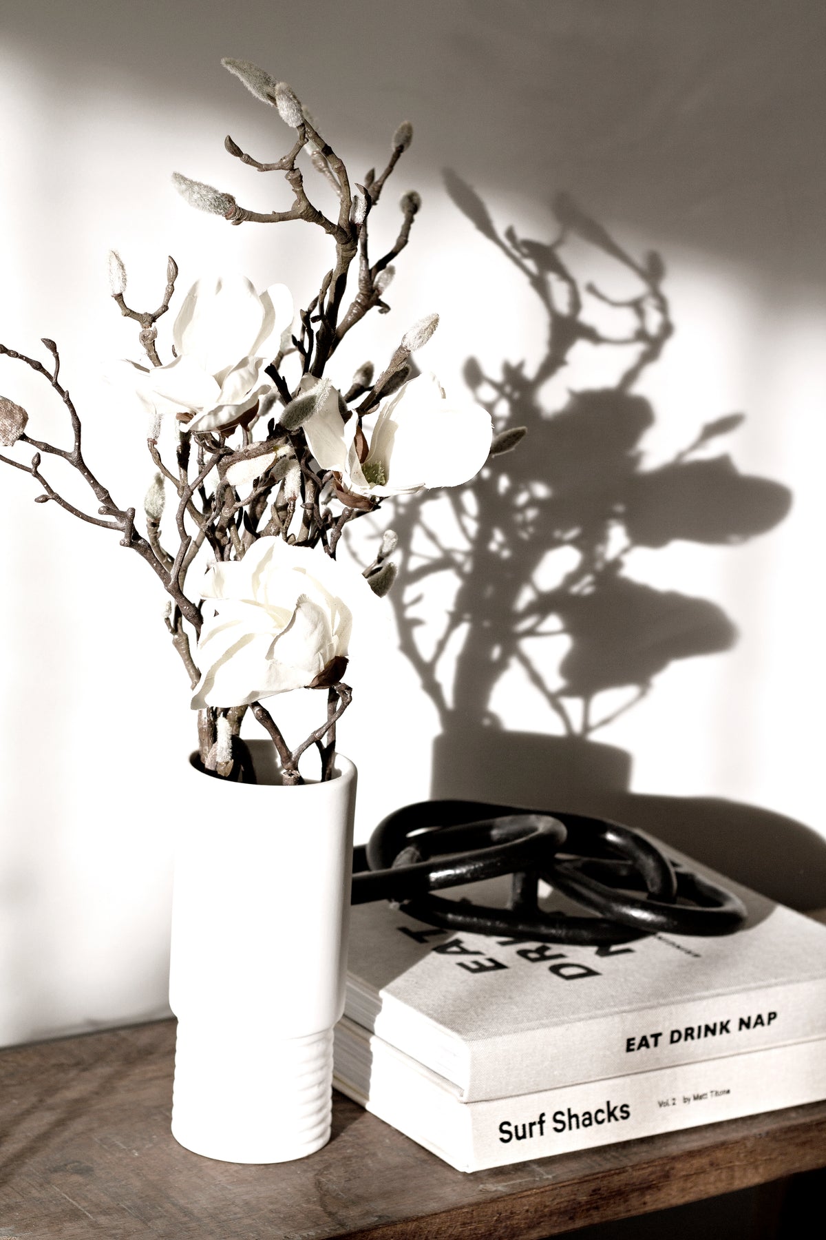 White vase of branches on the Eat, Drink, Nap book with a wick trimmer