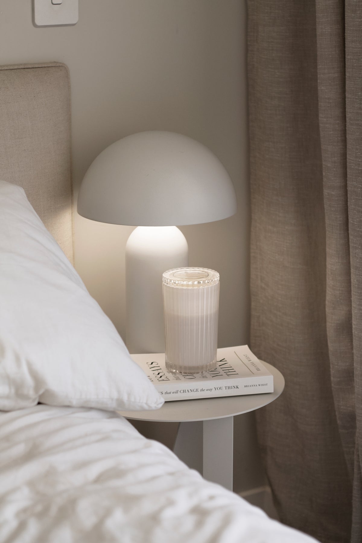 101 Essays That Will Change The Way You Think on a bedside table under a white mushroom lamp