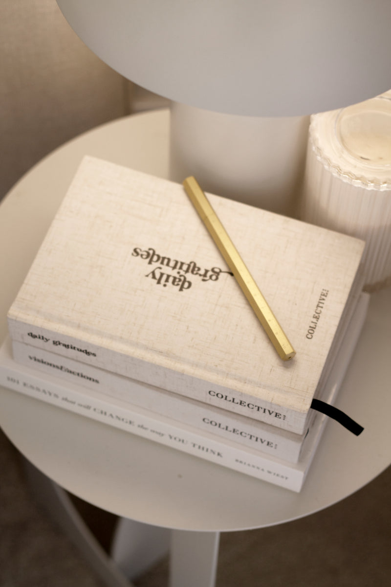 A limited edition Brass Reusable Pen from the Papier HQ stationery range, placed on a table alongside a lamp.