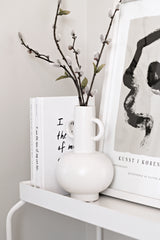 A modern white LOUIS VASE BLACK / WHITE from Ned Collections sits on a shelf next to a book.
