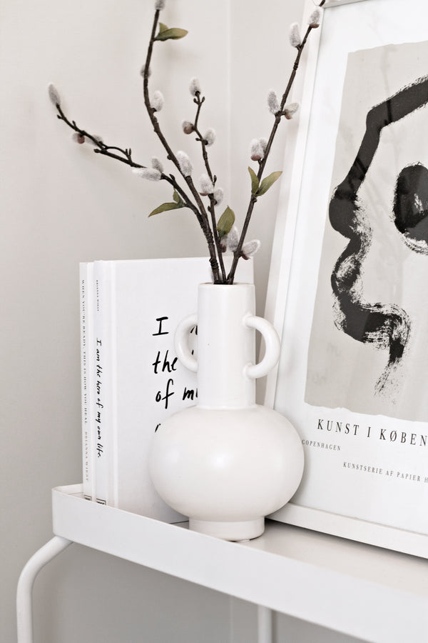 A modern white LOUIS VASE BLACK / WHITE from Ned Collections sits on a shelf next to a book.
