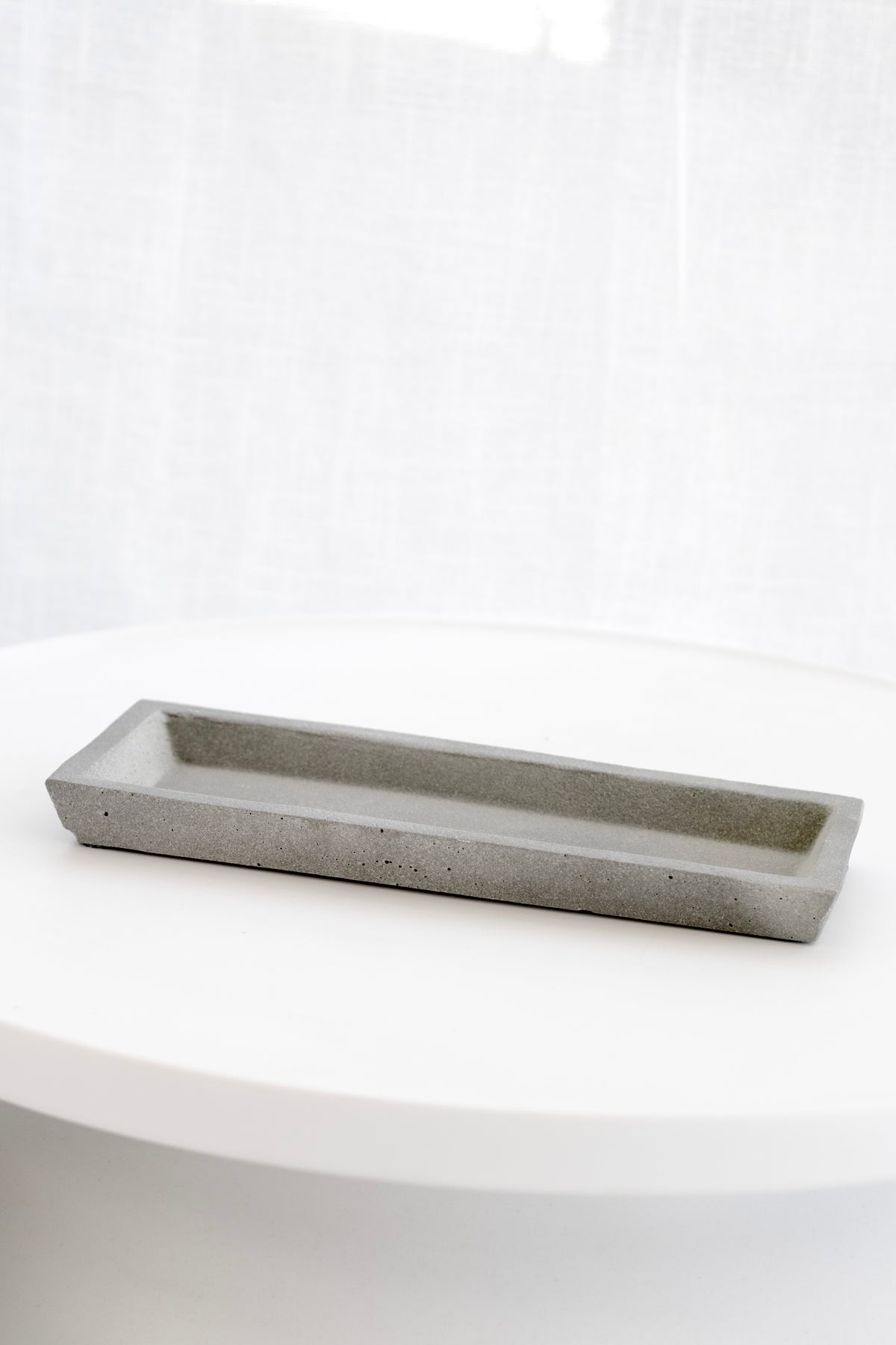 Empty Zakkia natural concrete tray on a round white side table