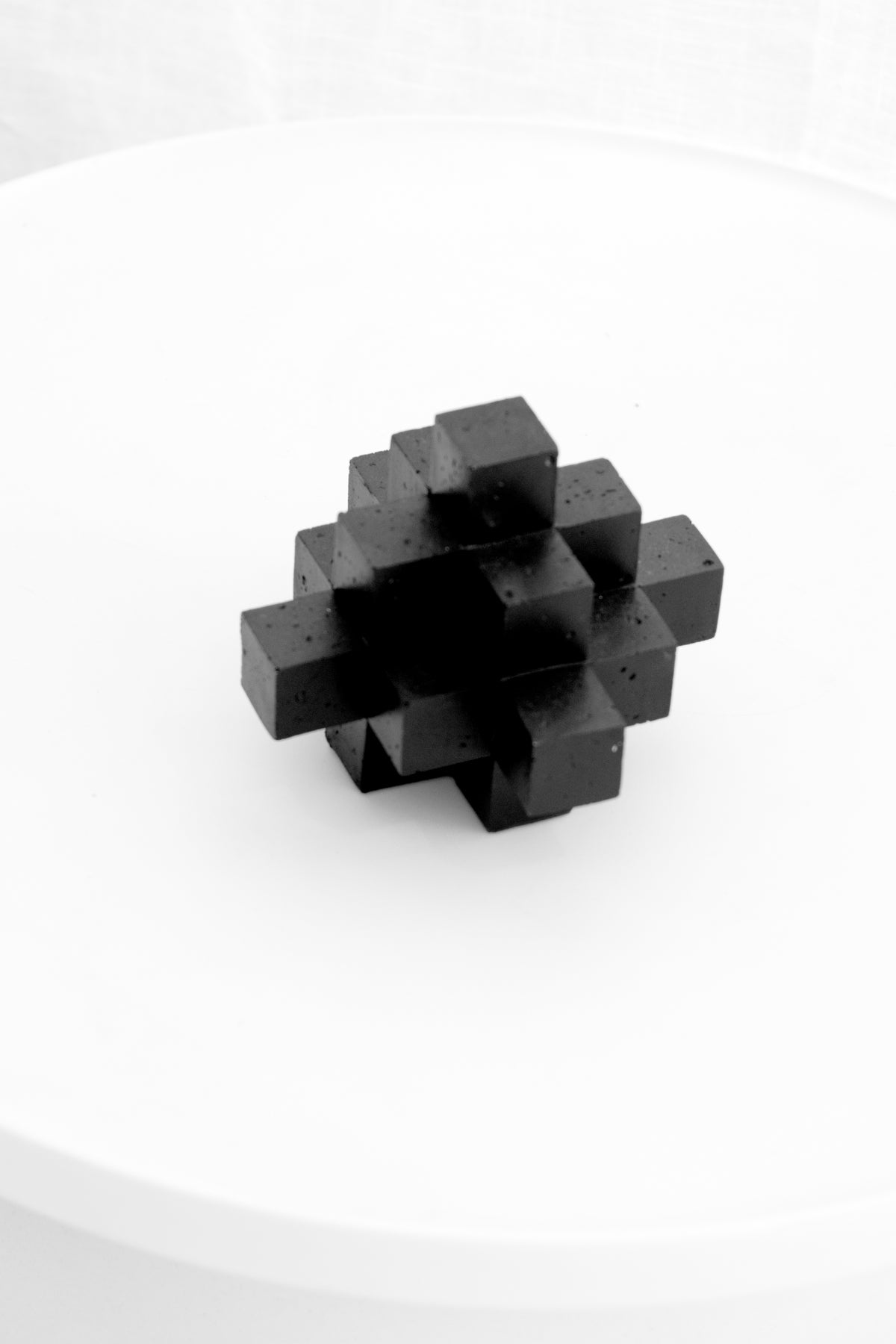 Small black Cubism sculpture on a white pedestal in soft light
