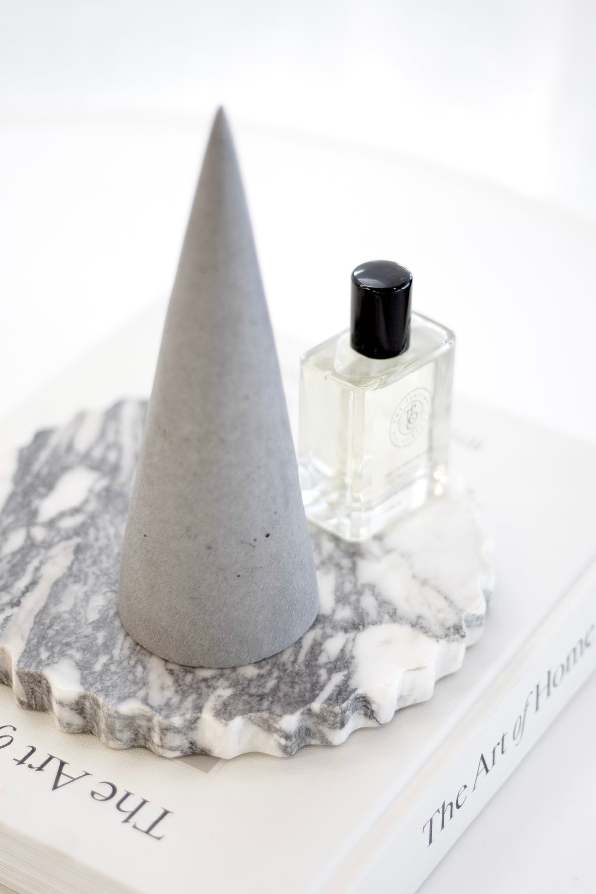 The Art of Home under a concrete cone and a perfume bottle on a marble petal-edge tray