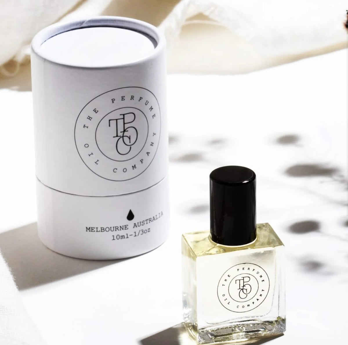 White perfume oil tube standing beside a roll-on bottle on a white plinth